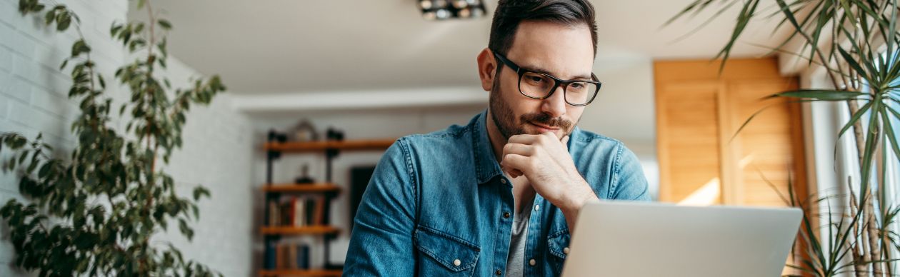 Bespectacled man looking seriously at his laptop