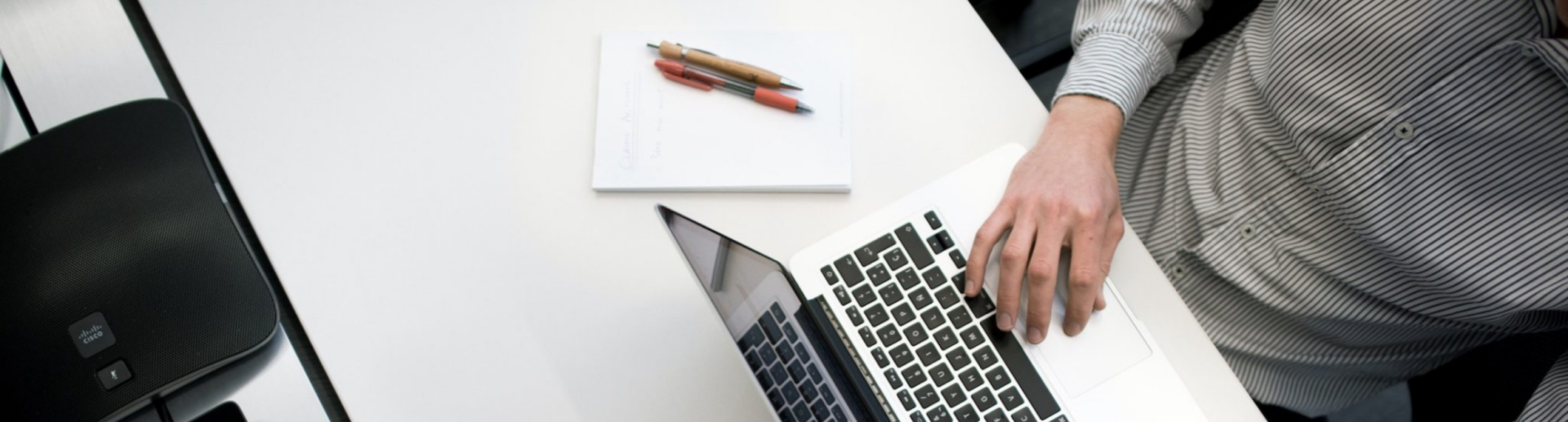 Image of a person sitting at a white desk typing on a laptop