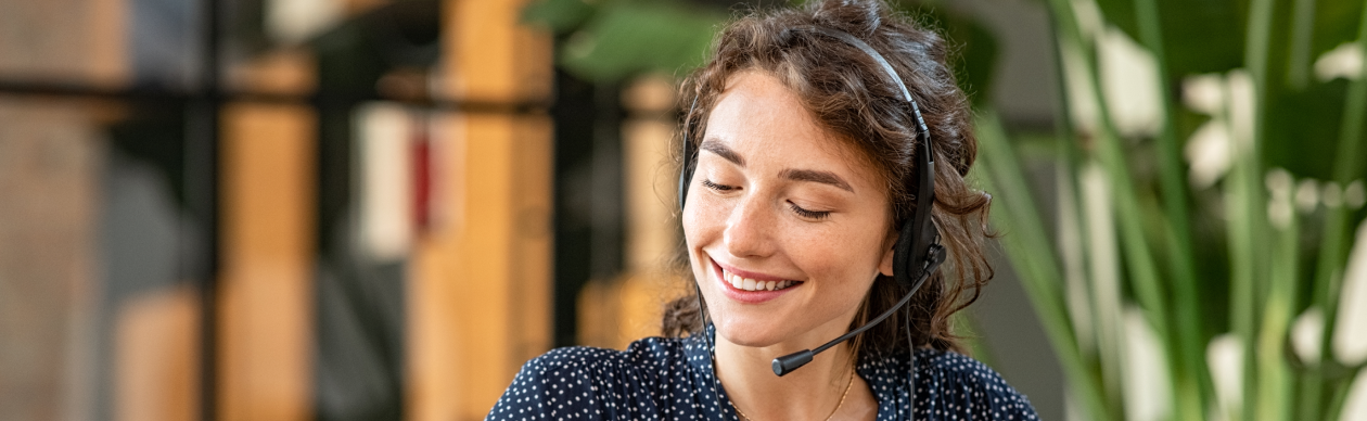 Woman with a phone headset smiling in front of a laptop