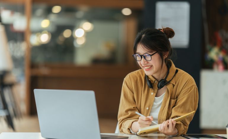 Bespectacled woman in and orange shirt smiling in front of a laptop