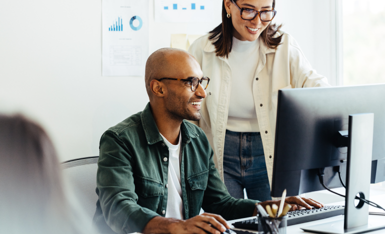 Two people chatting, one seated in front of a computer monitor