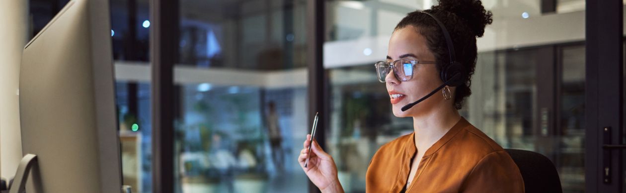 Woman in an orange shirt and phone headset in front of a computer monitor