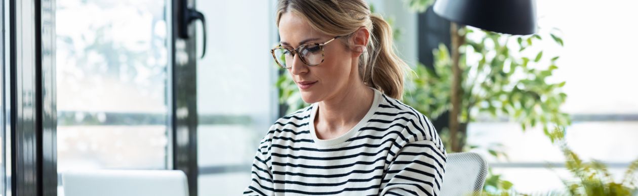 Woman in glasses and a striped shirt working on her laptop