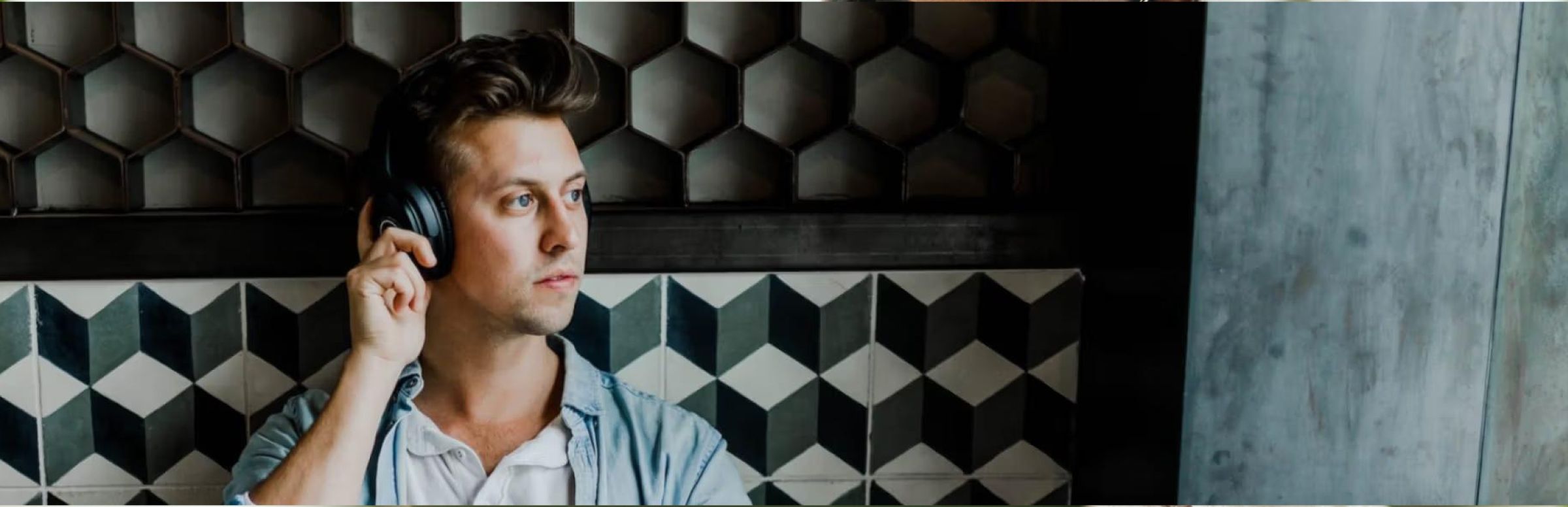 A person wearing headphones, looking contemplative, stands against a geometric-patterned wall. The tone is thoughtful, with a modern and stylish backdrop.