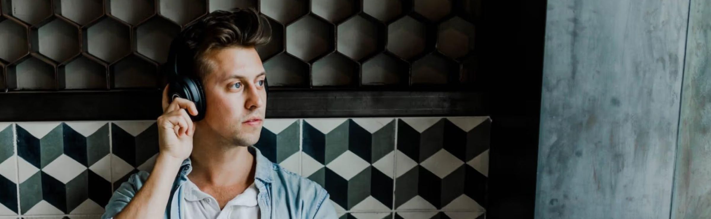 A person wearing headphones, looking contemplative, stands against a geometric-patterned wall. The tone is thoughtful, with a modern and stylish backdrop.