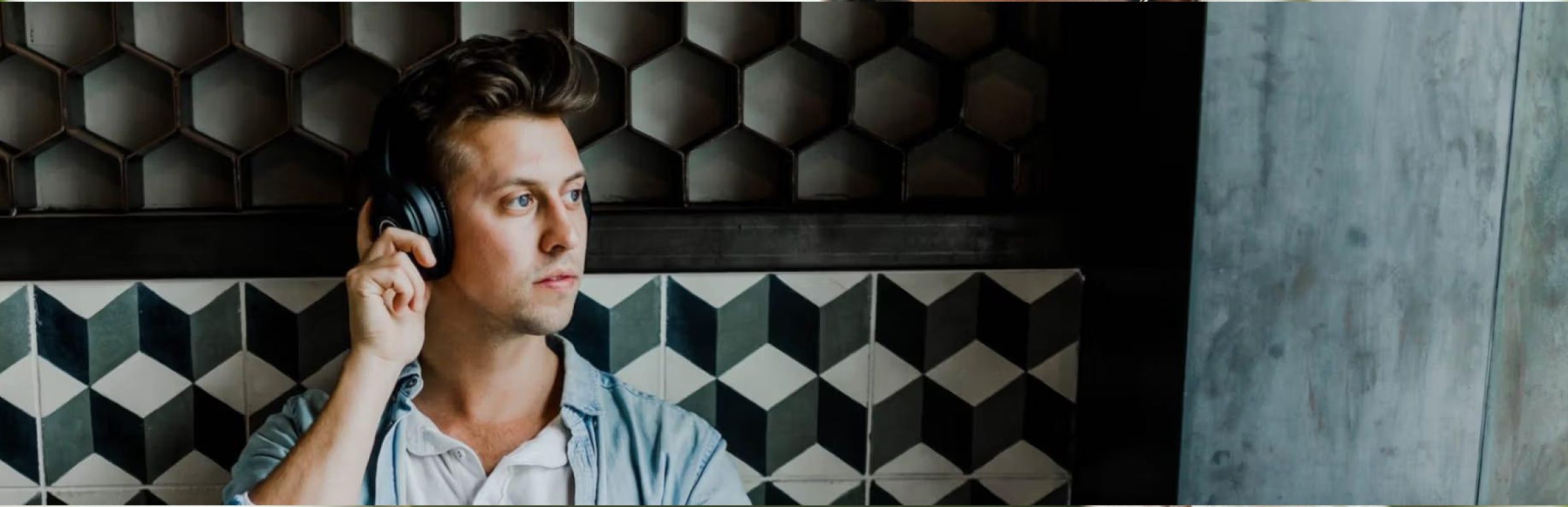 A person wearing headphones, looking contemplative, stands against a geometric-patterned wall. The tone is thoughtful, with a modern and stylish backdrop.