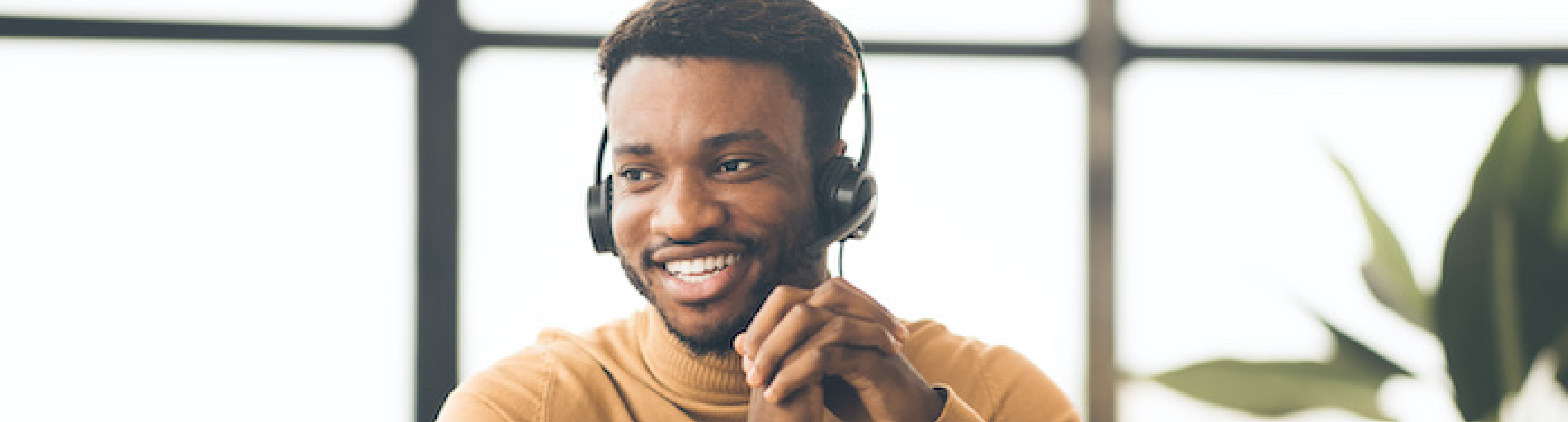 Man in an orange sweater smiling and wearing a phone headset