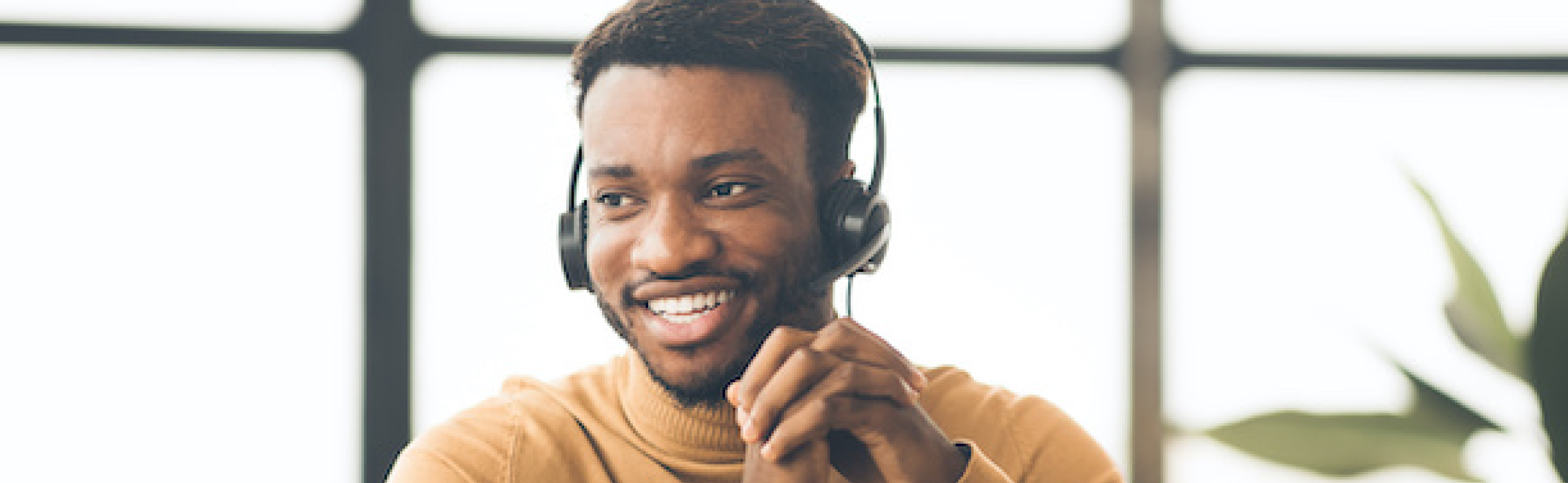 Man in an orange sweater smiling and wearing a phone headset