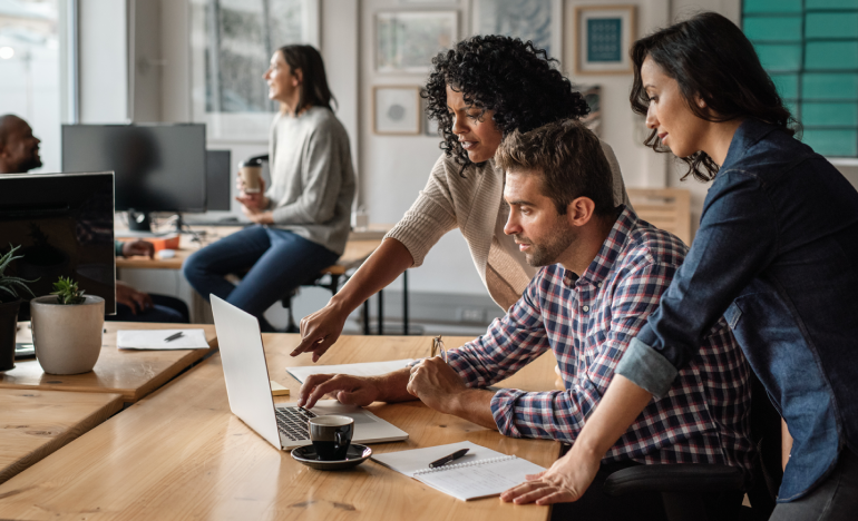 Three coworkers in an office discussing something on a laptop