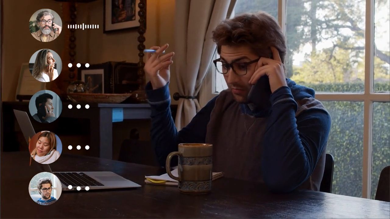 A man is on a phone call at a table with a laptop and coffee. He gestures with one hand, conveying frustration. Video call icons of four people are on the left.