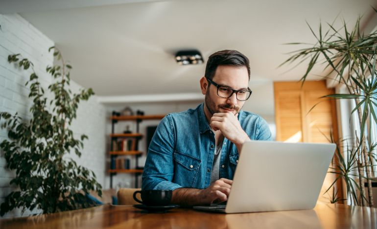 Bespectacled man looking seriously at his laptop