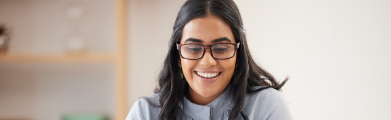 woman with glasses smiling while using her laptop