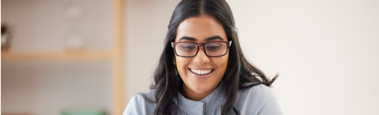 woman with glasses smiling while using her laptop