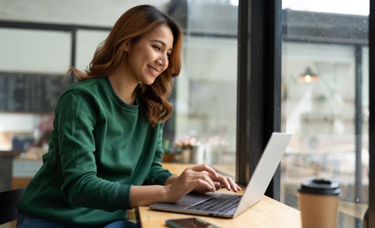 Woman in a green sweatshirt smiling at her laptop