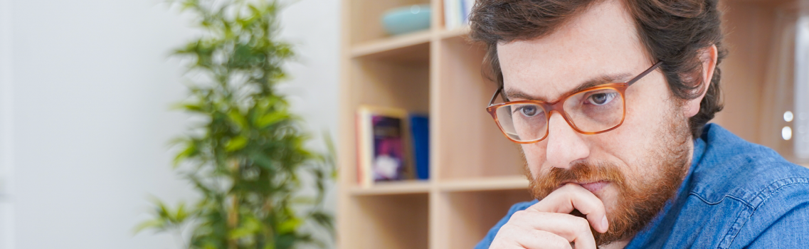 Bespectacled man looking seriously at a laptop