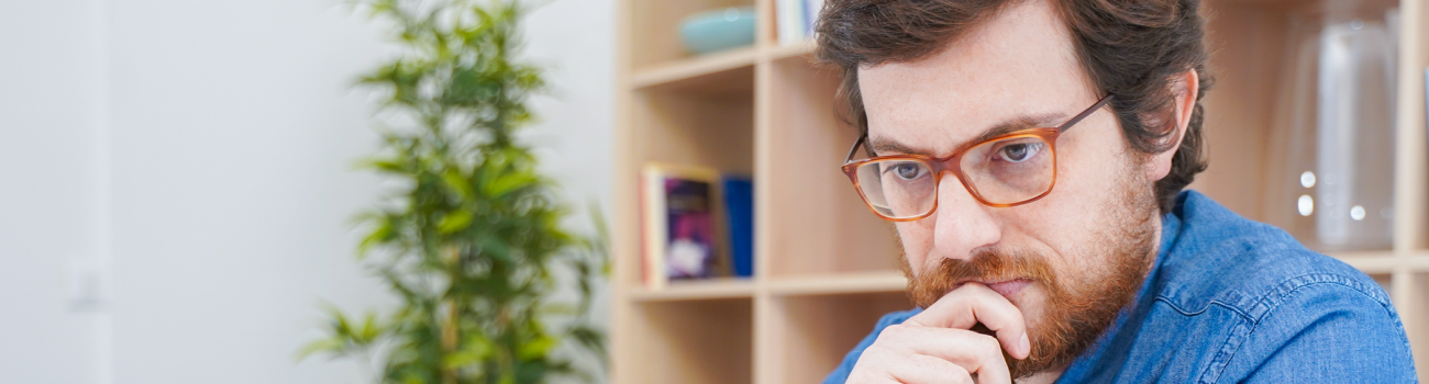 Bespectacled man looking seriously at a laptop