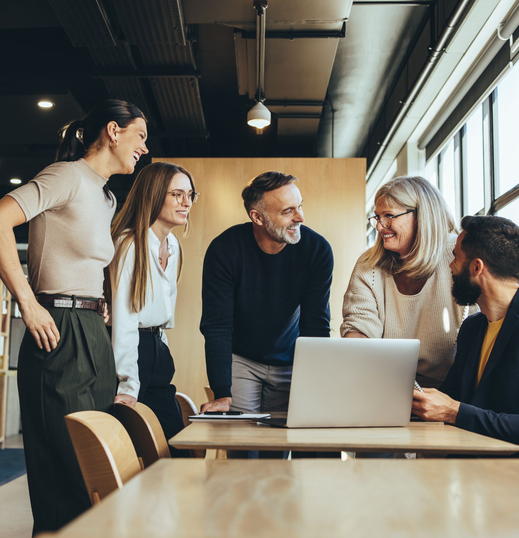 Image of office coworkers gathering over a laptop to have a discussion 