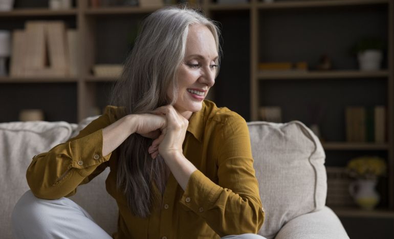 Older woman in a mustard-colored blouse smiling and seated in a living room
