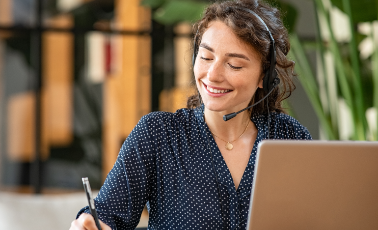Woman with a phone headset smiling in front of a laptop