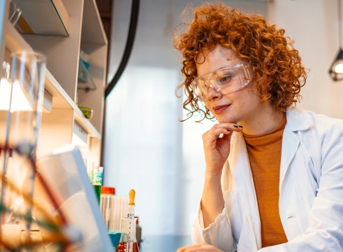 Scientist wearing safety goggles in a lab reviewing laptop