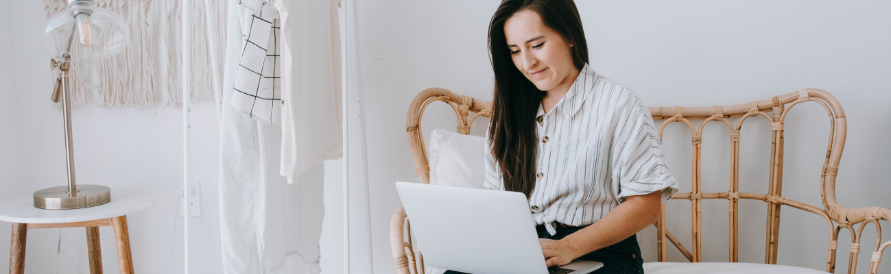 Woman seated on a wicker couch working on a laptop