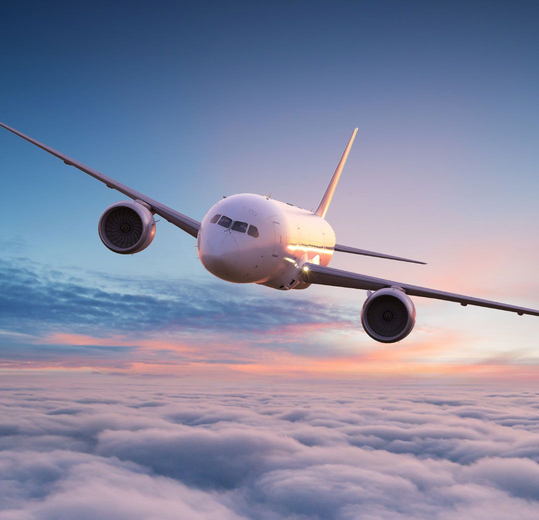 A large airplane soars above fluffy clouds at sunset, the sky painted in soft shades of pink and blue, evoking a sense of tranquility and freedom.