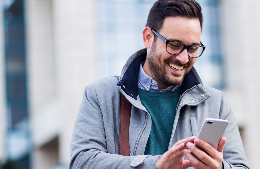 Man with glasses using his phone and smiling