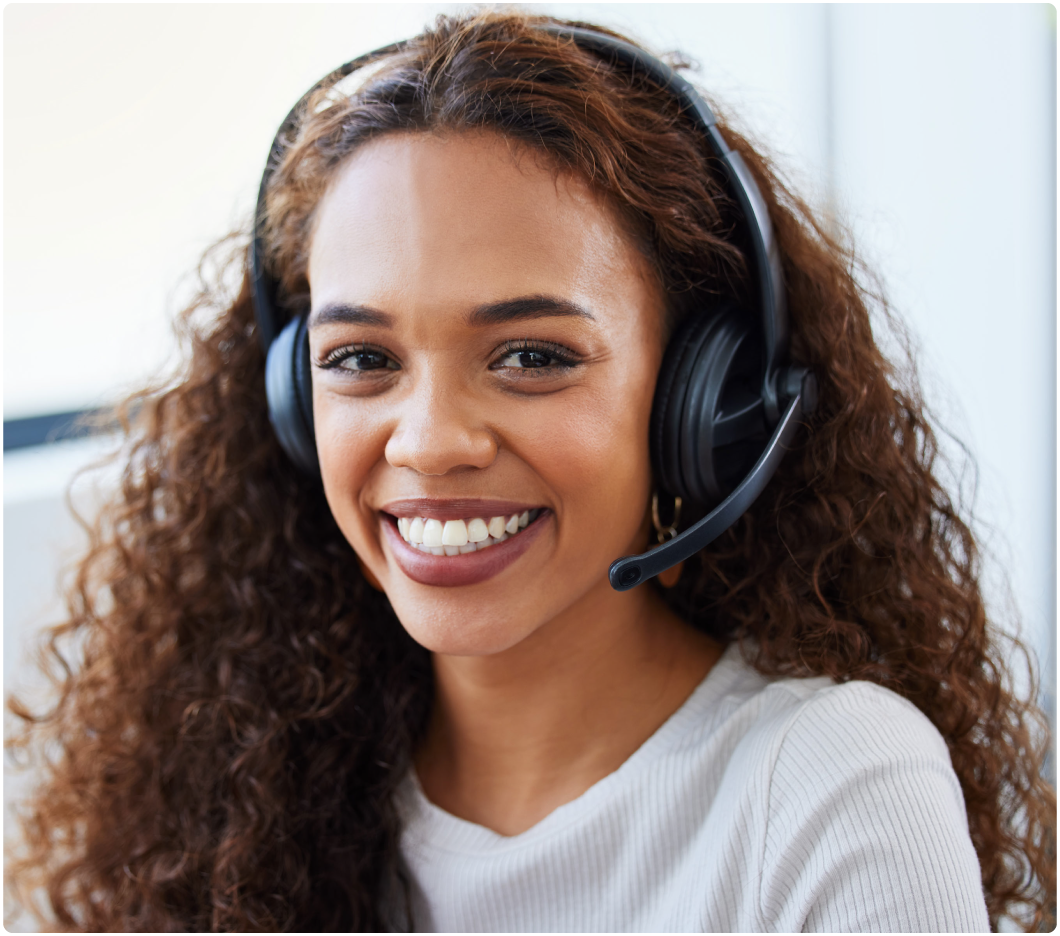 Smiling woman with curly hair wearing a headset, suggesting a customer service role, in a bright office setting, conveying friendliness and professionalism.