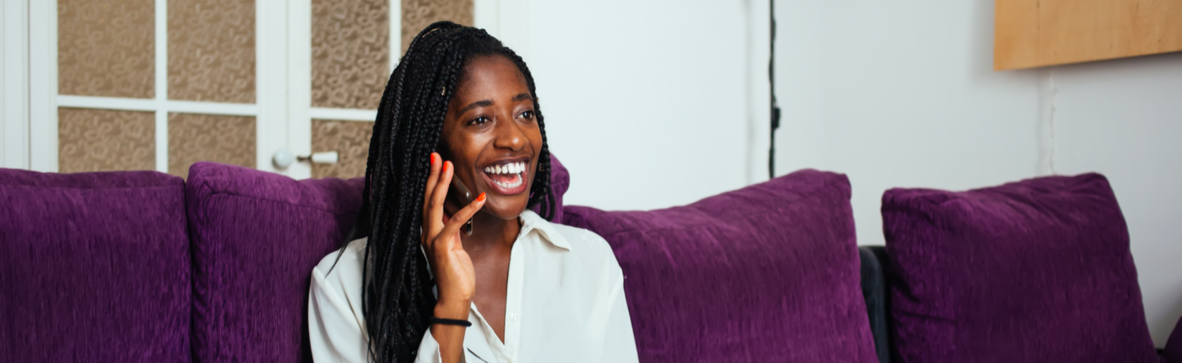 A woman sitting on a purple couch and talking on a cell phone