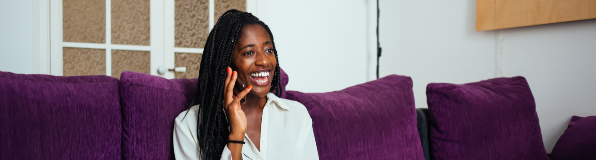 A woman sitting on a purple couch and talking on a cell phone