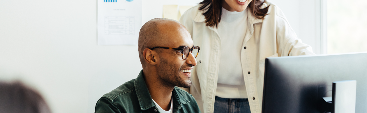 Two people chatting, one seated in front of a computer monitor