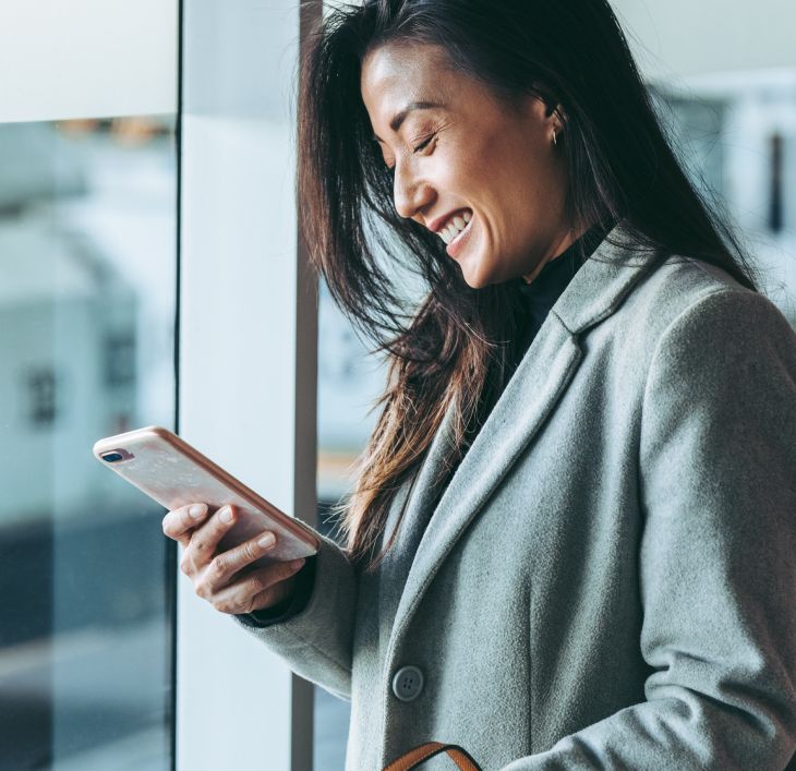 A woman smiling at her phone in an airport, holding a boarding pass. Chat bubbles show flight change confirmation, exuding convenience and satisfaction.