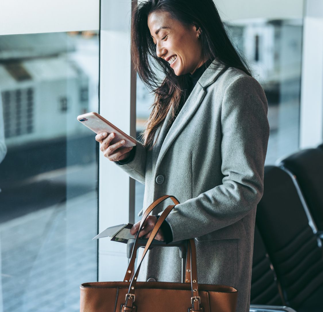 A woman smiling at her phone in an airport, holding a boarding pass. Chat bubbles show flight change confirmation, exuding convenience and satisfaction.