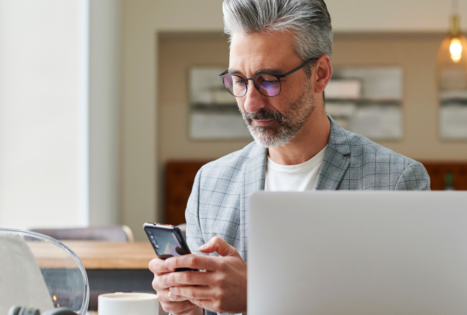 Bespectacled business man looking at his smartphone in front of a laptop