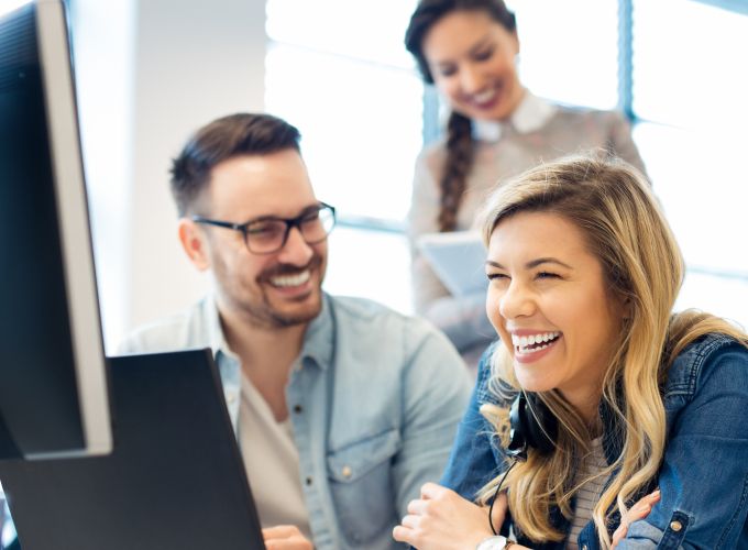 Three CX agents laughing while working side by side on laptops