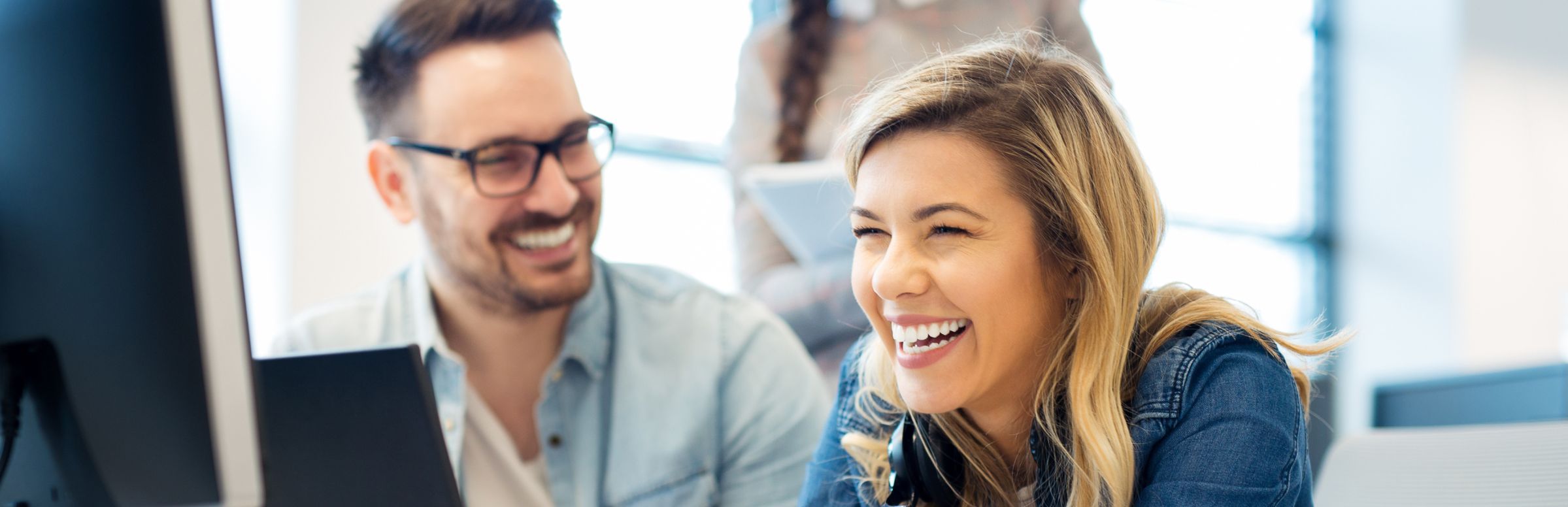 Two CX agents laughing while working side by side on laptops