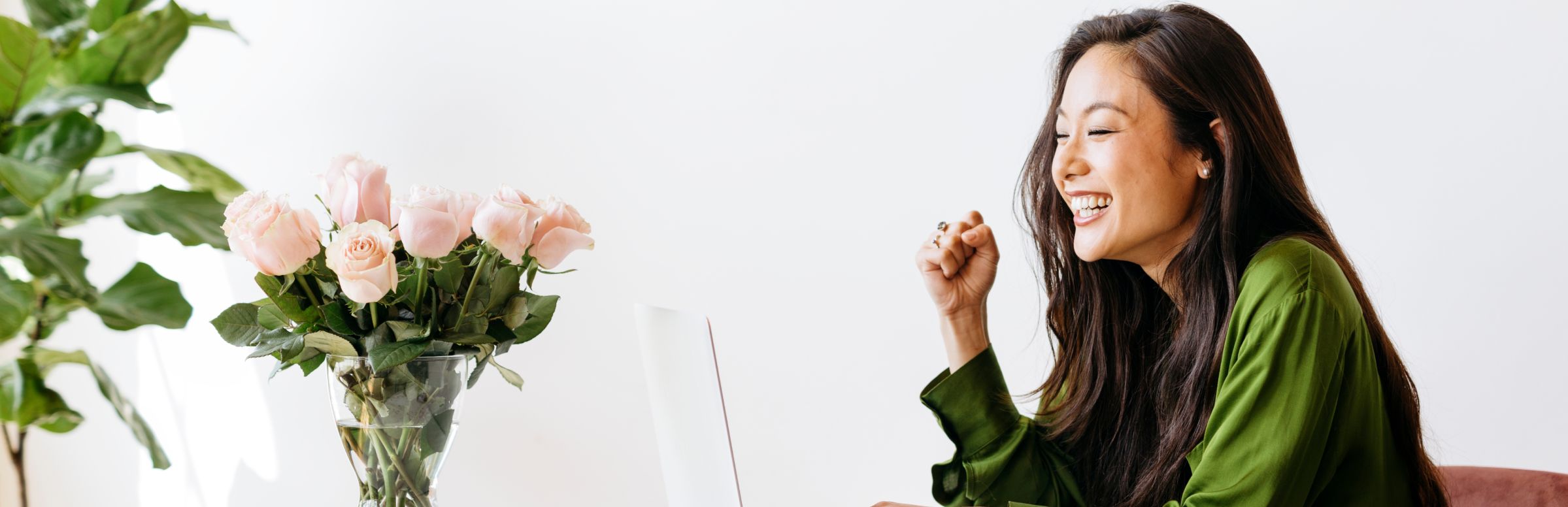 Woman at table with a vase full of flowers while on her laptop