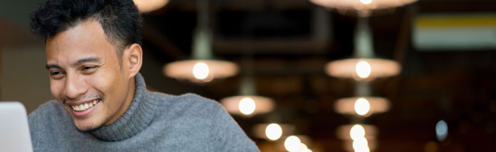 Man in a gray turtleneck smiling at a laptop