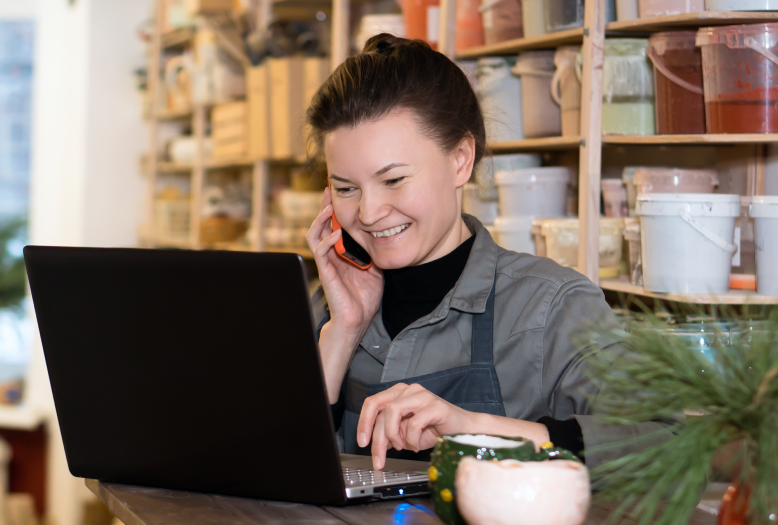 Smiling woman on a smartphone looking at a laptop