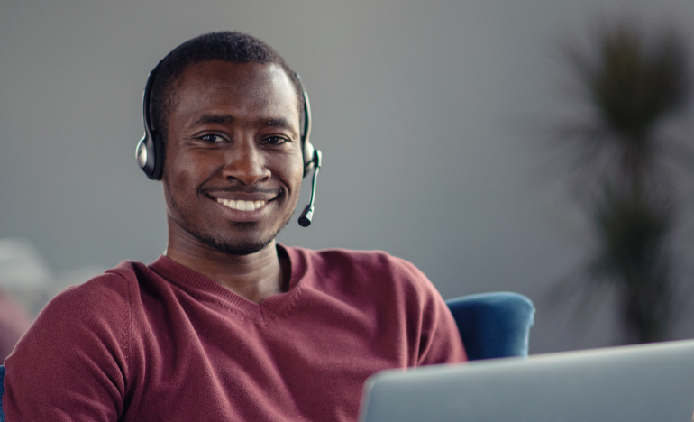 Smiling man in a red shirt with a phone headset working on a laptop