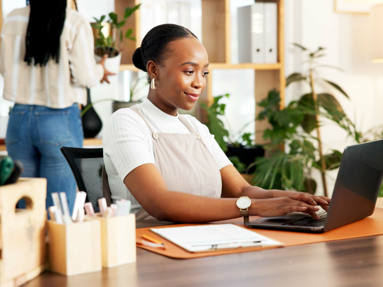 Small business owner working on a laptop at a plant-filled desk, managing her online store
