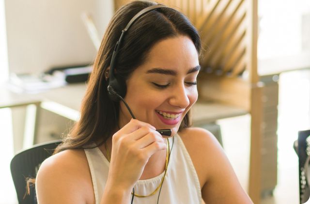 Woman in a white shirt smiling into a phone headset mic