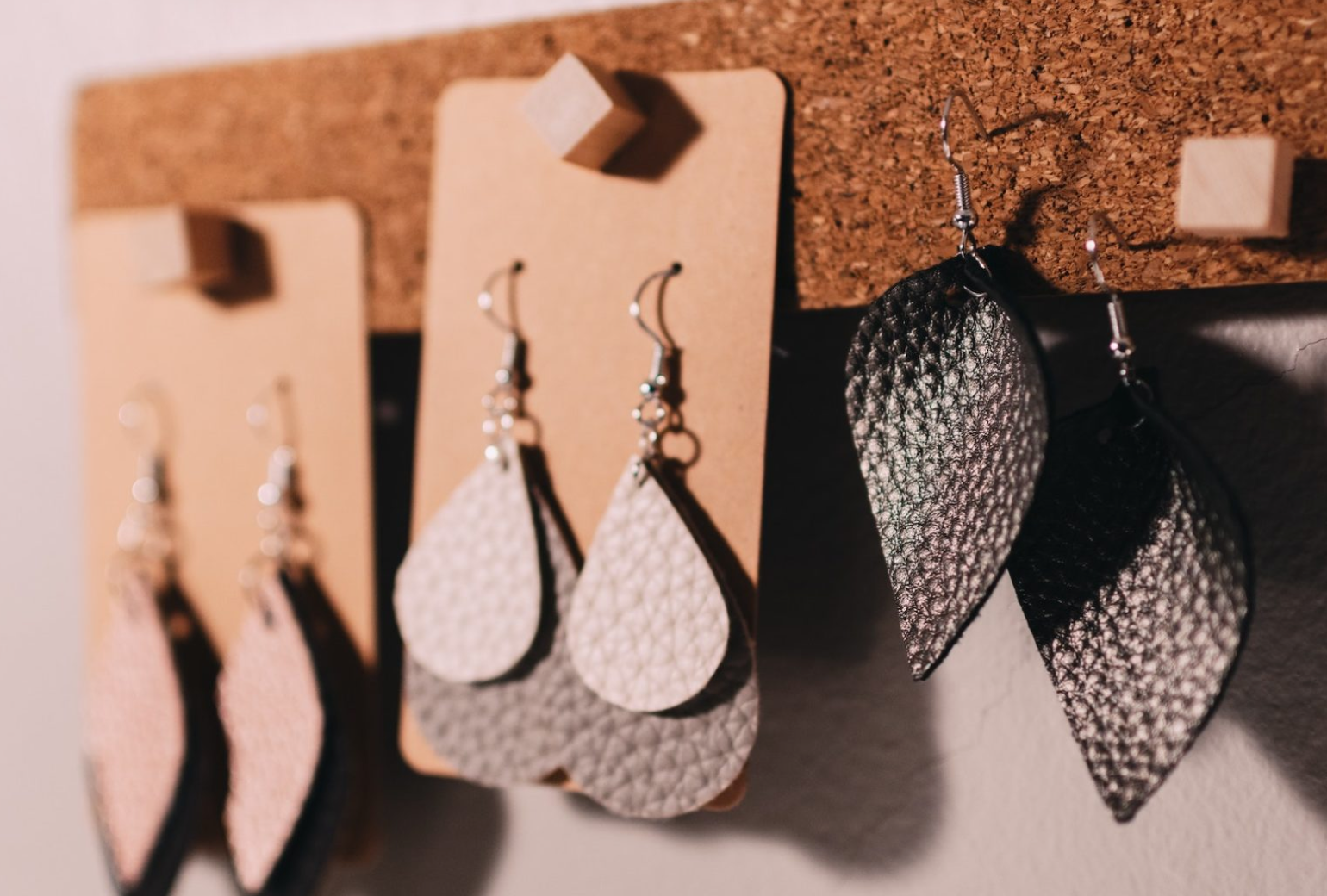 Three pairs of earrings hanging on a cork board