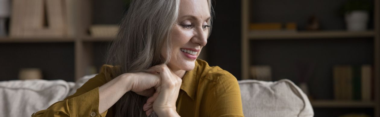 Older woman in a mustard-colored blouse smiling and seated in a living room