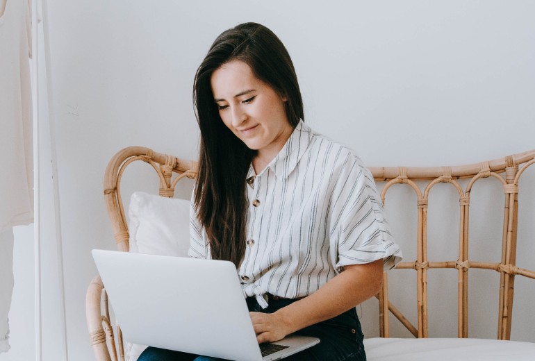 Woman seated on a wicker couch working on a laptop