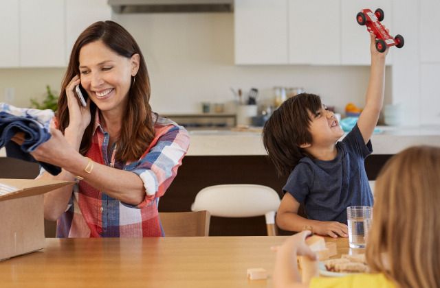 woman on the phone at the kitchen table with two of her kids