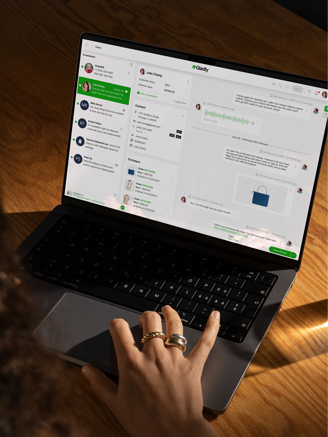 A person with rings on their fingers navigates a customer service chat platform on a laptop displaying conversations, orders, and customer details.