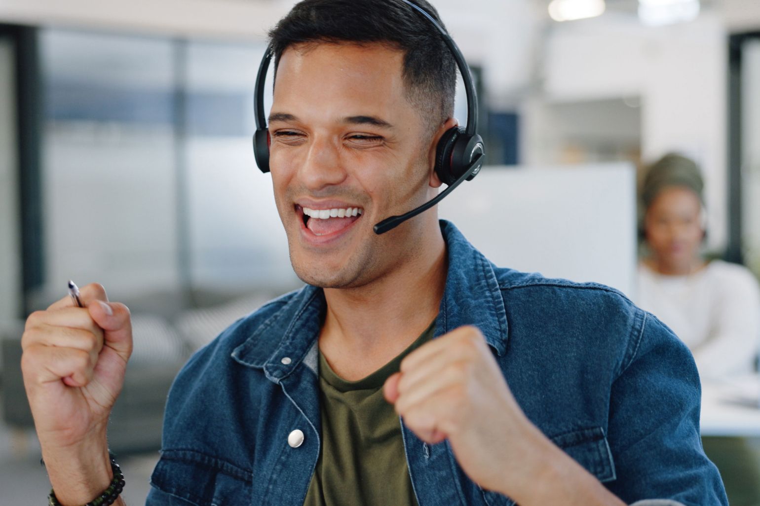 Customer service agent wearing headset cheering at his desk