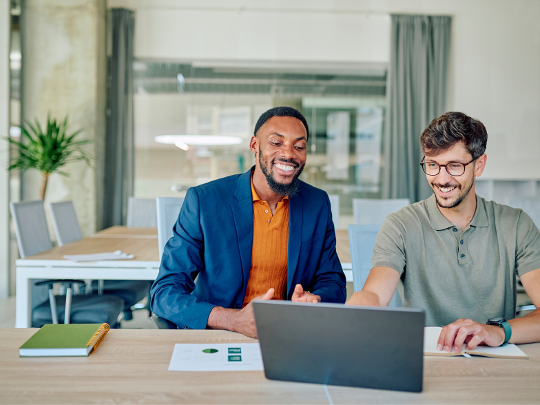 A support team manager and a team member collaborating over a laptop in a bright office, both smiling