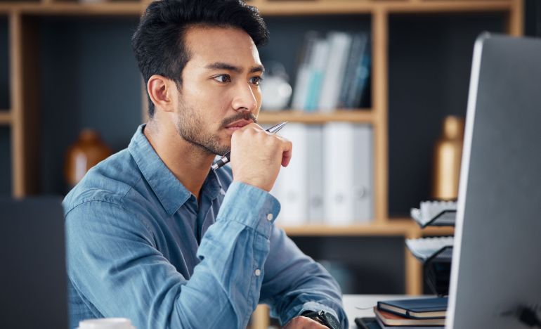 Man in a blue shirt looking seriously at his computer monitor